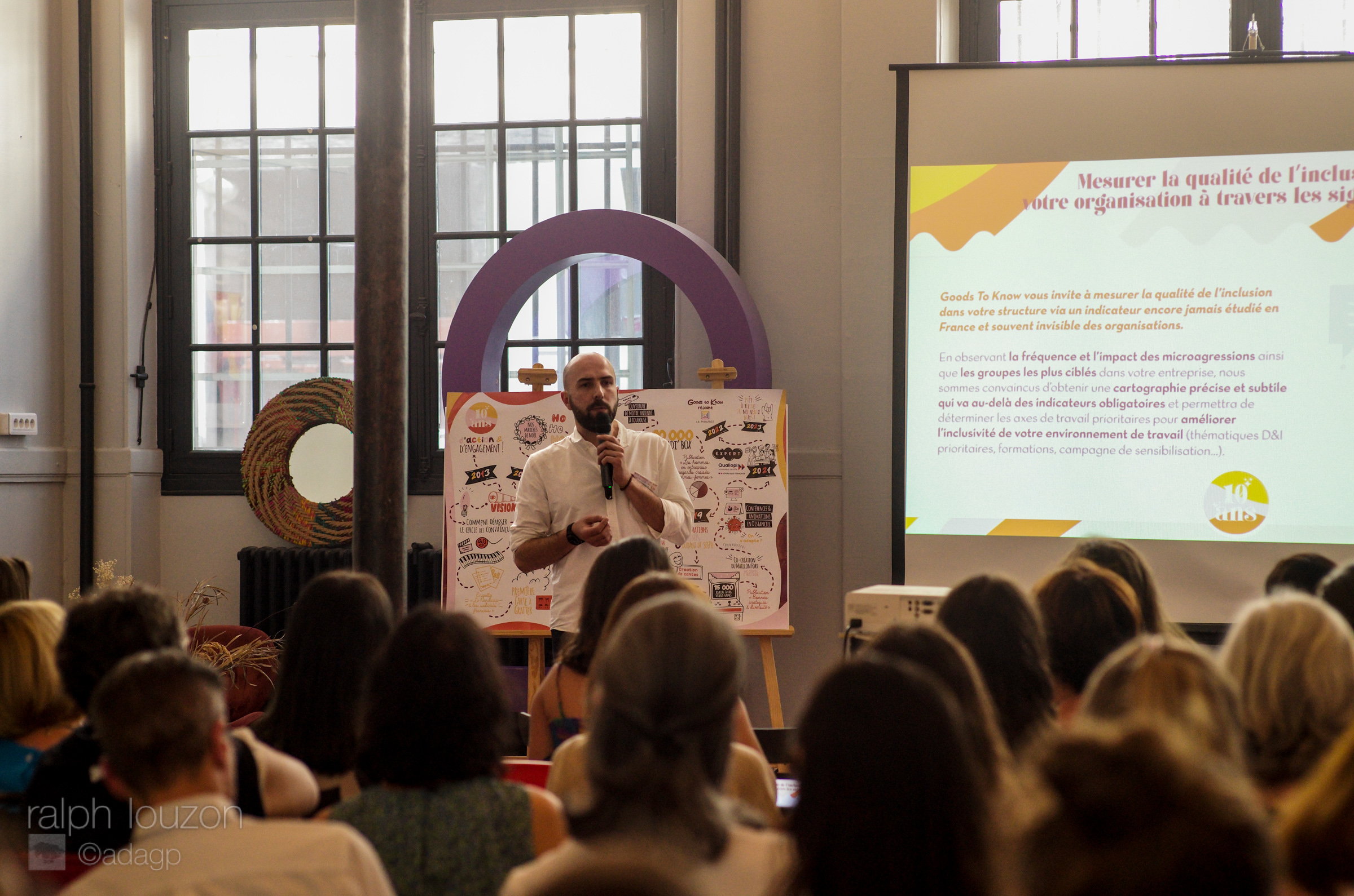 Jean Figarol à l'arrière plan tenant le micro, et la tête des invités de dos au premier plan